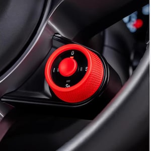 May include: Close-up of a red dial with a textured grip, set against a black interior. The dial has a central button and markings for '0', 'I', 'S', and 'S+'. The surrounding area is dark gray.