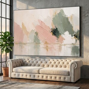 May include: A large rectangular canvas painting featuring abstract brushstrokes in shades of soft pink, sage green, cream, and gold. The artwork displays a textured, layered application of paint, creating a sense of depth and movement across the surface.