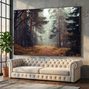 Könnte beinhalten: Ein großes rechteckiges Wandbild, das eine dichte Waldszene mit hohen Kiefern, einer nebligen Atmosphäre und einem mit goldbraunen Blättern bedeckten Boden zeigt, gerahmt in einem dünnen schwarzen Rand und montiert an einer strukturierten grauen Wand über einem beigen Sofa.