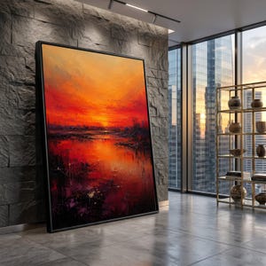 Op de afbeelding: Een groot rechthoekig ingelijst schilderij met een levendig zonsonderganglandschap in intense tinten oranje, rood en dieppaars. Het kunstwerk toont een horizonlijn boven een reflecterend wateroppervlak met textuur.