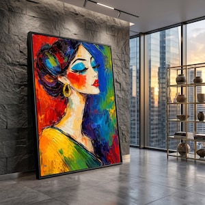 May include: A framed abstract painting of a woman's profile. The artwork uses bold brushstrokes and vibrant colours, including red, blue, yellow, and green. The woman has blue eyeshadow, red lipstick, and gold earrings. The painting is displayed in a modern interior.