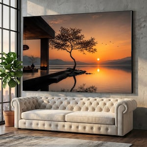 Puede incluir: Un gran cuadro rectangular que muestra una puesta de sol sobre un lago tranquilo con un árbol solitario en una plataforma de hormigón, colgado sobre un sofá beige capitoné. A la izquierda, una planta verde en maceta junto a una ventana.