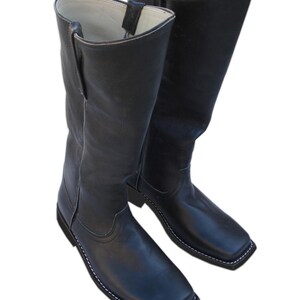 May include: A pair of black leather cowboy boots with a square toe and white stitching. The boots have a tall shaft and a pull tab at the top. The boots are made of a smooth, shiny leather.