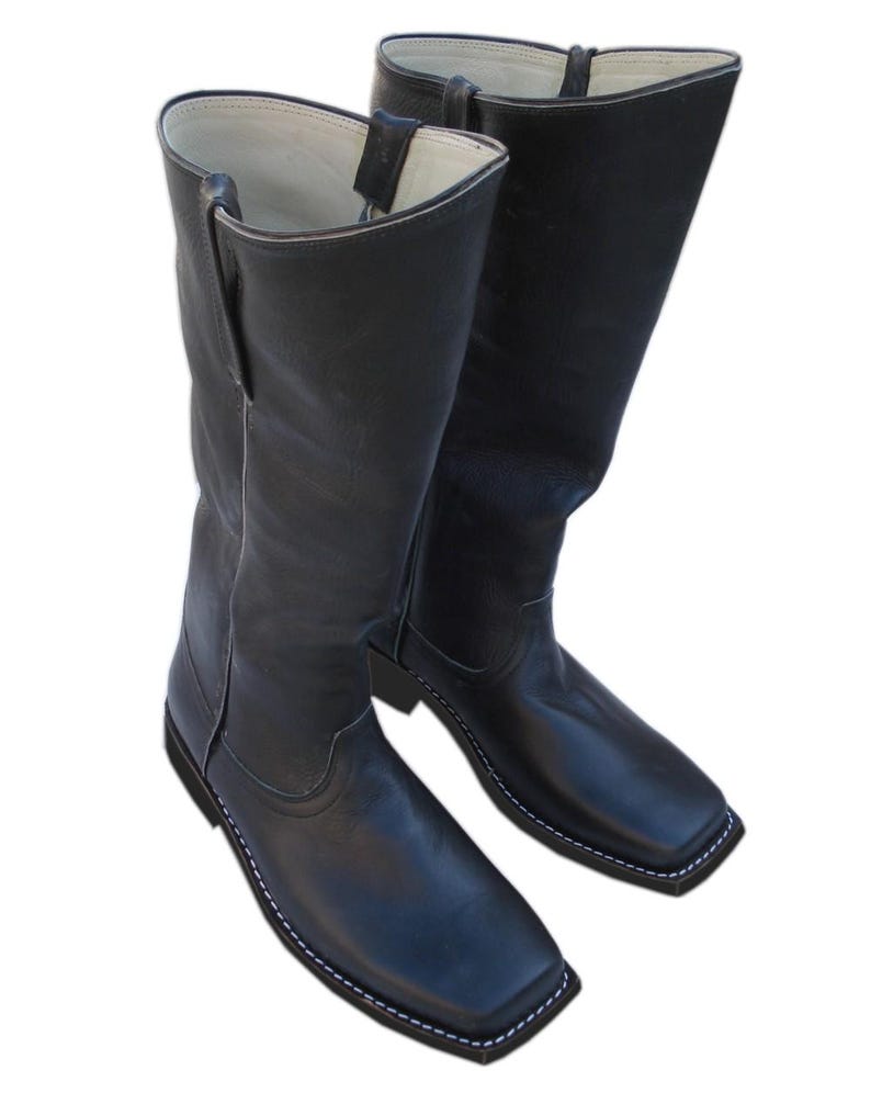 May include: A pair of black leather cowboy boots with a square toe and white stitching. The boots have a tall shaft and a pull tab at the top. The boots are made of a smooth, shiny leather.