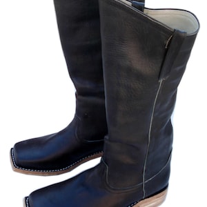 May include: A pair of black leather cowboy boots with square toes. The boots have a tall shaft, a light-colored sole, and white stitching around the sole. The boots are made of a smooth, textured leather.