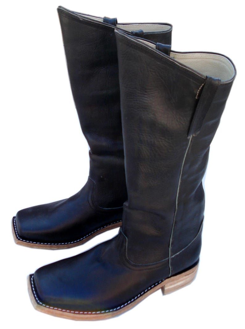 May include: A pair of black leather cowboy boots with square toes. The boots have a tall shaft, a light-colored sole, and white stitching around the sole. The boots are made of a smooth, textured leather.