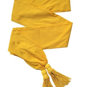 Könnte beinhalten: Ein goldgelbes Band mit zwei passenden Quasten. Das Band ist aus geripptem Stoff gefertigt und in Zickzackform gefaltet. Die Quasten sind am Ende des Bandes verknotet.