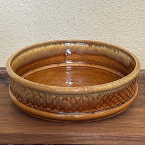 May include: A round, brown ceramic bowl with a textured, diamond-patterned band around the middle. The bowl has a glossy finish and a wide rim. The interior is a lighter shade of brown.