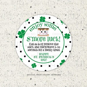 Op de afbeelding: Een witte cirkel met zwarte stippen en groene klavertjes aan de rand. In het midden van de cirkel staat een cartoonafbeelding van een s'more met de tekst "enjoy some s'more luck!"  Eet zoals het is of verwijder de stok en verwarm het 5-10 seconden in de magnetron voor een smeltende traktatie. Fijne St. Patricksdag!