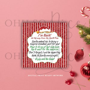 Peut inclure: Carte imprimable à rayures rouges et blanches avec une illustration de Père Noël. Le texte dit "Je suis de retour ! Tout le chemin du pôle Nord. Le Père Noël m'a demandé d'apporter une boule de neige magique juste pour toi ! Verse 230 à 290 ml de lait chaud sur le dessus et attends la surprise. N'oublie pas, je vais faire mon rapport au Père Noël tous les soirs. Profite et sois sage !"