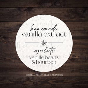 Op de afbeelding: Rond wit label met zwarte tekst die "OHH SO homemade vanilla extract OHH SO ingredients vanilla beans & bourbon OHH SO" luidt, met een sneeuwvlok als afbeelding. Het label heeft een houtnerf achtergrond.