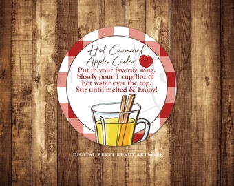 May include: A red and white gingham circle with the text "Hot Caramel Apple Cider" and an illustration of a mug with cinnamon sticks and apple cider. The text below the title reads "Put in your favourite mug. Slowly pour 1 cup/8oz of hot water over the top. Stir until melted & Enjoy!"