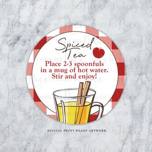 Op de afbeelding: Een witte cirkel met een rood-wit geruite rand. De tekst "Spiced Tea" is geschreven in zwarte cursieve letters. Een rode appel met een groen blad staat naast de tekst. De tekst "Place 2-3 spoonfuls in a mug of hot water. Stir and enjoy!" is geschreven in zwarte letters. Een glazen mok met een gele vloeistof en twee kaneelstokjes is afgebeeld in het midden van de cirkel. De tekst "DIGITAL PRINT READY ARTWORK" is geschreven in zwarte letters onderaan de cirkel.