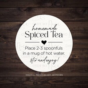 Op de afbeelding: Een ronde, witte sticker met de tekst "homemade Spiced Tea" in een decoratief lettertype. Instructies luiden: "Doe 2-3 lepels in een mok heet water. Roer en geniet!" Een zwart hart is gecentreerd boven de instructies.
