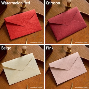 May include: Four colorful envelopes in watermelon red, crimson, beige, and pink. Each envelope is 112mm x 161mm. The envelopes are displayed on a wooden surface. The envelopes are for stationery and correspondence.