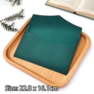 May include: A dark green envelope, measuring 22.8 x 16.1cm, lies open on a light brown wooden tray. The envelope has a pointed flap. The tray is square with rounded edges. The text "Size: 22.8 x 16.1cm" is at the bottom of the image.