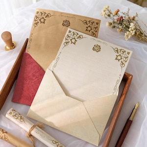 May include: Stationery set featuring cream and brown paper with decorative floral corner designs and a rose emblem. Includes lined paper, envelopes, and a red envelope. A wooden tray, pen, and wax seal are also present.