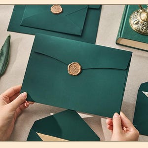 May include: Dark green envelopes with gold wax seals. The envelopes are rectangular with a flap closure. Several envelopes are visible, some overlapping. A decorative feather pen is in the background. The wax seals have an ornate design.