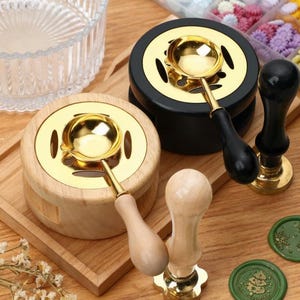 Op de afbeelding: Een verzameling waszegelstempels. Bevat twee wassmeltovens met goudkleurige kommen en houten handvatten, twee waszegelstempels en verschillende groene waszegels met decoratieve ontwerpen. De items zijn gerangschikt op een houten oppervlak.