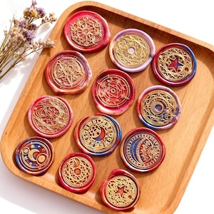 Op de afbeelding: Een verzameling decoratieve waszegels met ingewikkelde gouden ontwerpen, waaronder sterren, manen en geometrische patronen. De zegels zijn in tinten rood, blauw en goud, gerangschikt op een houten dienblad.