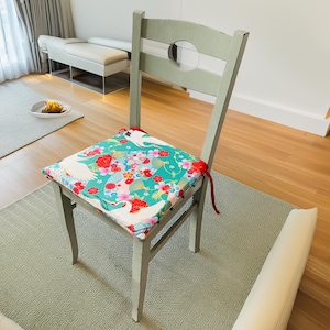 May include: A green chair with a floral patterned cushion. The cushion features white birds and red flowers on a green background. The chair is made of wood and has a light green finish.