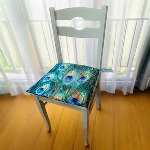 May include: A white wooden chair with a peacock feather patterned cushion. The chair is in front of a window with white curtains.
