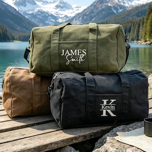 Op de afbeelding: Drie canvas reistassen in olijfgroen, bruin en zwart. De olijfgroene tas is voorzien van de witte tekst "JAMES SMITH". De zwarte tas toont een grote letter "K" met de naam "Kevin" in het midden. Elke tas is uitgerust met handvatten en riemen.