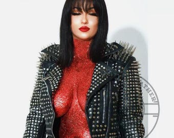 May include: A black leather jacket with silver studs and spikes. The jacket has a zipper closure and a collar. The model is wearing a red sparkly top.
