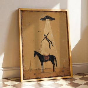 May include: A framed wall art print featuring a desert landscape with a black horse and a cowboy being abducted by a flying saucer. The cowboy is suspended in a beam of light above the horse, with the text "HELP!" written near the figure.