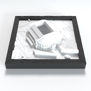 Op de afbeelding: Een driedimensionaal wit architecturaal model van een stadion in een vierkante zwarte lijst. Het model toont een gedetailleerd reliëf van de stadionstructuur, inclusief de tribunes en het dak, omringd door een vereenvoudigd stratenplan.
