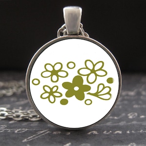 Pode incluir: Colar com pingente prateado com um berloque redondo. O berloque apresenta um fundo branco e um desenho floral verde-oliva. O colar tem uma corrente fina.