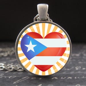 May include: A silver necklace with a round pendant featuring a heart-shaped design with the Puerto Rican flag colours. The heart is surrounded by orange and white sun rays.