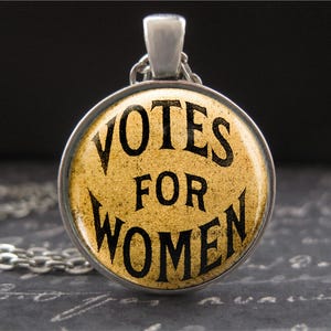 以下が含まれることがあります： 黄色い背景に黒い文字で「Votes for Women」と書かれた丸いペンダントが付いた銀色のネックレスです。