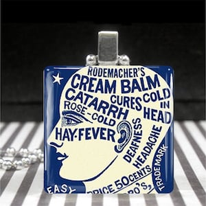 May include: A blue and white glass pendant with a vintage advertisement for "Rodemacher's Cream Balm" that claims to cure cold, catarrh, rose-cold, hay fever, deafness, and headache. The text "Price 50 Cents" is visible at the bottom of the pendant.