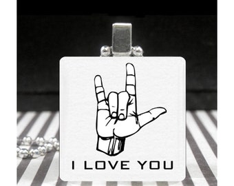 May include: A white square pendant necklace with a black and white image of the American Sign Language sign for "I love you". The pendant also has the words "I LOVE YOU" printed below the image.