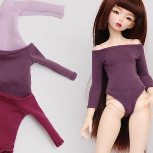 May include: Three long-sleeved shirts in different shades of purple. The shirts are made of a soft, stretchy fabric and have a fitted silhouette. The shirts are shown on a doll with long brown hair.