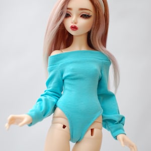 May include: A doll with long, pink-tinted hair and a white headband. The doll wears a turquoise off-the-shoulder bodysuit. The doll has a fair complexion, red lips, and is posed with arms slightly outstretched.