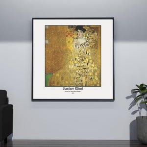 May include: A framed print of a painting by Gustav Klimt titled "Portrait of Adele Bloch-Bauer I". The painting features a woman in a gold dress with a geometric pattern. The background is a gold and black abstract design.