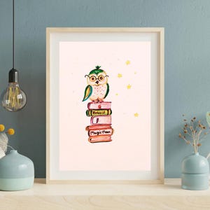 Könnte beinhalten: Ein gerahmter Aquarelldruck mit einer skurrilen Eule mit Brille, die auf einem Stapel Bücher sitzt. Die Bücher sind mit "Hobbit" und "Magic Moon" beschriftet. Gelbe Sterne sind im Hintergrund verstreut. Das Kunstwerk ist vor einem hellrosa Hintergrund.