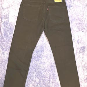 Op de afbeelding: Zwarte denim jeans met een klassiek vijf-zakken ontwerp. De jeans hebben een rood label op de achterzak en een leren patch. De jeans liggen plat op een patroon oppervlak.