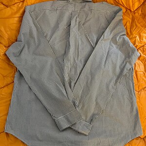 May include: A long-sleeved button-down shirt with a classic black and white gingham pattern. The shirt is laid flat, showcasing the collar, button placket, and cuffs. The fabric appears to be a lightweight cotton or blend, suitable for casual wear.