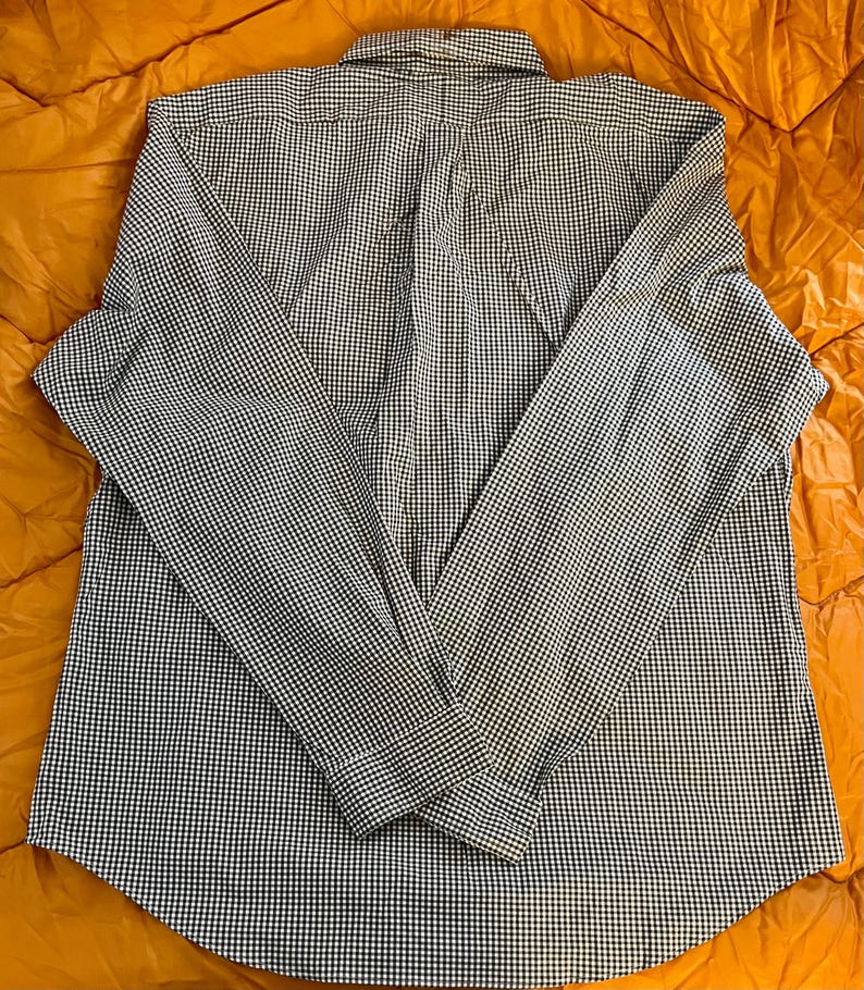 May include: A long-sleeved button-down shirt with a classic black and white gingham pattern. The shirt is laid flat, showcasing the collar, button placket, and cuffs. The fabric appears to be a lightweight cotton or blend, suitable for casual wear.