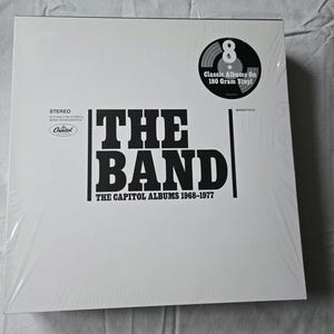 May include: White box with black text that reads "The Band The Capitol Albums 1968-1977". A black and white record label with the text "Classic Albums On 180 Gram Vinyl" is in the upper right corner.