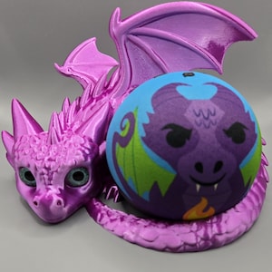 May include: A purple dragon figurine with outstretched wings holds a blue and purple ball. The dragon has detailed scales, wings, and a long tail. The ball features a dragon face design with green and orange accents.
