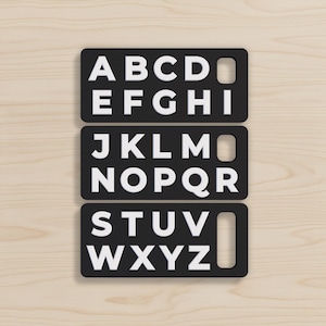 May include: Three rectangular black plaques featuring white embossed capital letters of the English alphabet. Each plaque contains a series of letters arranged in rows, with a vertical rectangular cutout on the right side of each black panel.