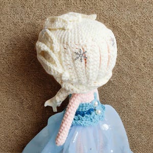 Pu&ograve; includere: Bambola fatta a mano con testa e capelli all'uncinetto color crema, ornata da un dettaglio a fiocco di neve. La bambola ha un vestito azzurro con gonna in tulle e collo all'uncinetto rosa. Giocattolo per bambini.