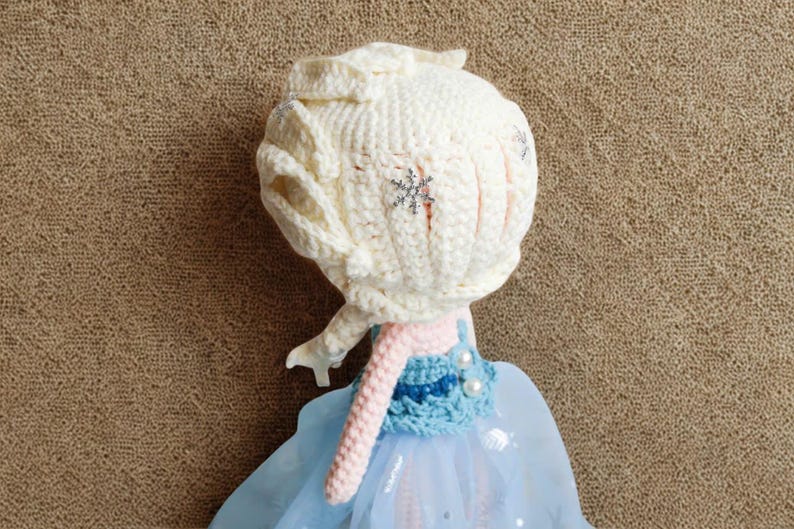 Pu&ograve; includere: Bambola fatta a mano con testa e capelli all'uncinetto color crema, ornata da un dettaglio a fiocco di neve. La bambola ha un vestito azzurro con gonna in tulle e collo all'uncinetto rosa. Giocattolo per bambini.