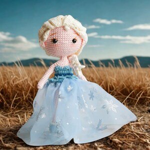 Pu&ograve; includere: Bambola all'uncinetto fatta a mano di una principessa, con viso rosa chiaro, capelli biondi e un vestito blu con dettagli a fiocco di neve. La bambola &egrave; ambientata su uno sfondo di erba alta e cielo blu.
