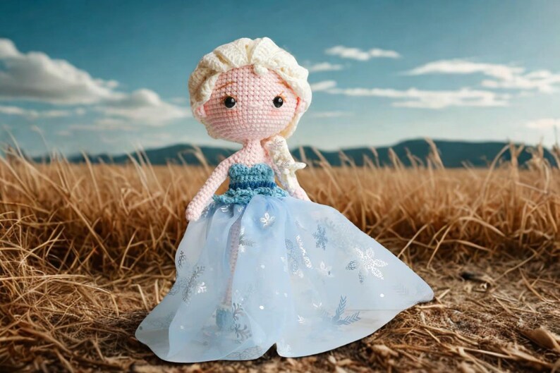 Pu&ograve; includere: Bambola all'uncinetto fatta a mano di una principessa, con viso rosa chiaro, capelli biondi e un vestito blu con dettagli a fiocco di neve. La bambola &egrave; ambientata su uno sfondo di erba alta e cielo blu.