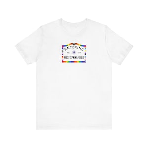 Puede incluir: Camiseta blanca con un gráfico colorido. El gráfico dice "ENTERING WEST SPRINGFIELD INC. 1774" con un borde de arcoíris y un diseño de bandera arcoíris.